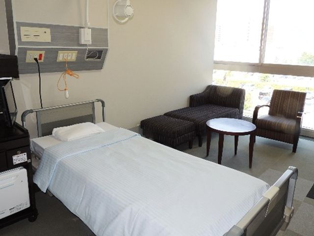 窓際の個室ベッド 居室   窓から光が入る、家具付きの落ち着いた個室です。ベッドのそばに椅子と丸い机があり、くつろぎやすい雰囲気です。