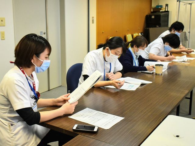 職員の会議室 多目的室   マスクを着けた職員の方々がテーブルを囲み、資料を見ながら打ち合わせをしています。落ち着いた空間で、連携して働く様子が伝わります。
