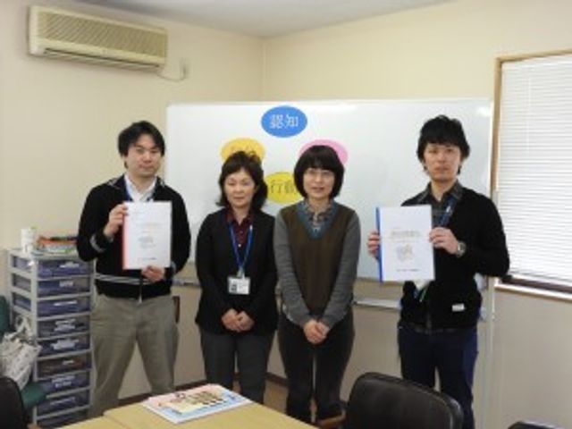 スタッフ集合の居室 居室   書類を手にしたスタッフの皆さんが並んでいます。明るい室内で、打ち合わせや記録確認の場面が想像しやすいです。