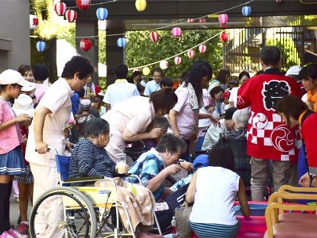 行事風景の外観 中庭 和やかな雰囲気の行事です。屋外で、お子様からお年寄りまで一緒に談笑している様子が見て取れます。