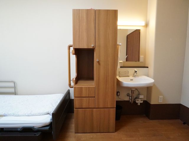 居室のベッドと洗面台 居室 余裕を持った設計の居室では、快適な住空間が確保されています。個室内に洗面台があり、日々の生活がより便利になっています。