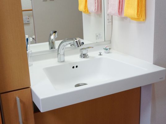 清潔感あふれる真っ白な洗面台には、シャワー水栓が取り付けられている。右端に、ピンクとオレンジ色のタオルが掛けてある。