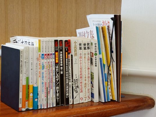 木目調デザインのテーブルの右端に、色々なジャンルの雑誌がブックエンドに挟んで立ててある。左端の本には、カラフルな帯が付いている。