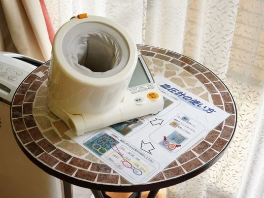 ベージュ色と茶色のタイルでデザインされた丸い台の上に、血圧計と使い方が書かれた紙が置いてある。左横には、白い家電製品がある。