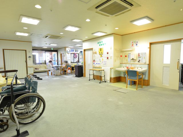 広々とした共用スペース ホールの介護用車椅子 スタッフが優しく対応しており、利用者は落ち着いた時間を過ごしています。広々とした共有スペースでは、日常生活にゆとりを感じられそうです。