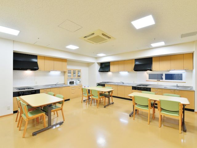 明るい食堂 食堂   広めの食堂にテーブルと椅子が整然と配置され、落ち着いて過ごしやすい雰囲気です。壁付けのキッチンもあり、作業しやすそうなつくりです。