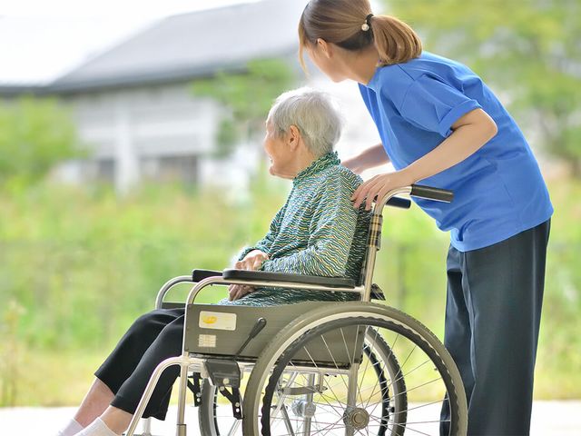 車椅子の高齢者と介助 庭 心地よい自然光の下、高齢者と介助スタッフが穏やかに過ごしています。緑豊かな環境でリラックスできます。