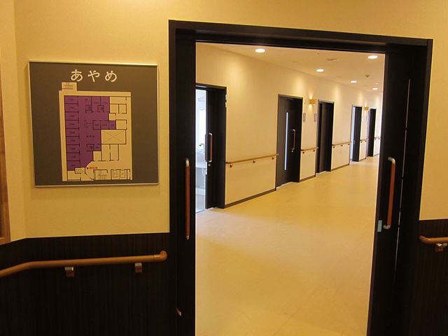 ゆったり通路と掲示板 廊下 手すり付きの広い通路が、利用者様の快適な移動をサポートします。壁には施設の案内板も設置されています。