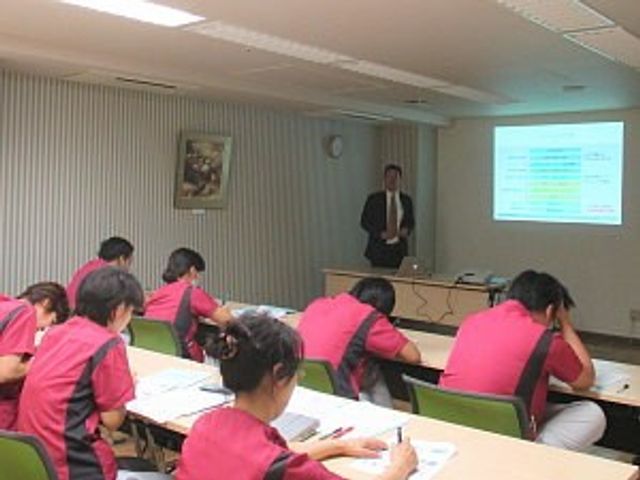 研修中の会議室 多目的室   机に向かって学ぶ様子が見られる広い多目的室です。スクリーンを使って説明を行っており、研修の場として活用されています。