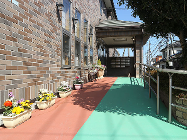 緑あふれる建物のエントランス 手すりを設置した安全なアプローチ 心地よい緑に囲まれたエントランスは、訪れる方に安らぎを提供しております。スタッフとの出会いの場としても最適です。