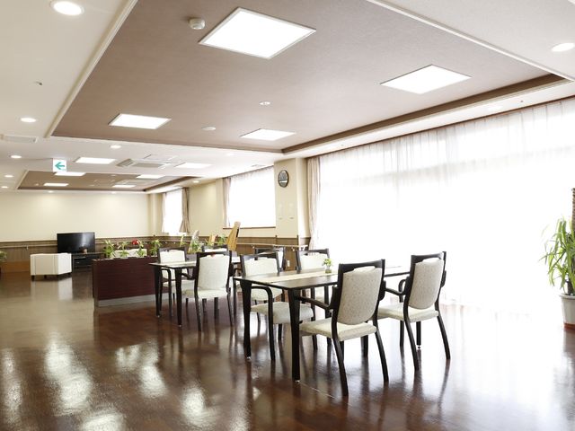 広々とした快適なダイニング 共同リビングで演奏会 明るく開放的なダイニングスペースで、ゆったりとした食事の時間を楽しめる環境です。木目調のテーブルや椅子が温かみのある雰囲気を作り出しています。