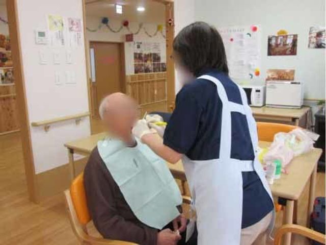 ケアスタッフと利用者の食事支援 口内ケア スタッフが優しく食事のお手伝いをしている様子が伝わります。コミュニケーションを大切にした温かいケアが特徴です。