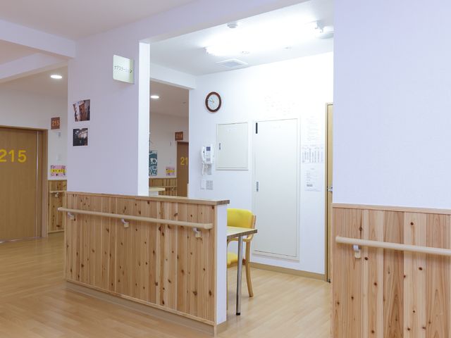 木目調のナチュラルな廊下 受付 清潔な木目の手すりや座席が設けられた廊下です。皆さんが落ち着いた雰囲気の中で日々をお過ごしいただける環境が整っています。