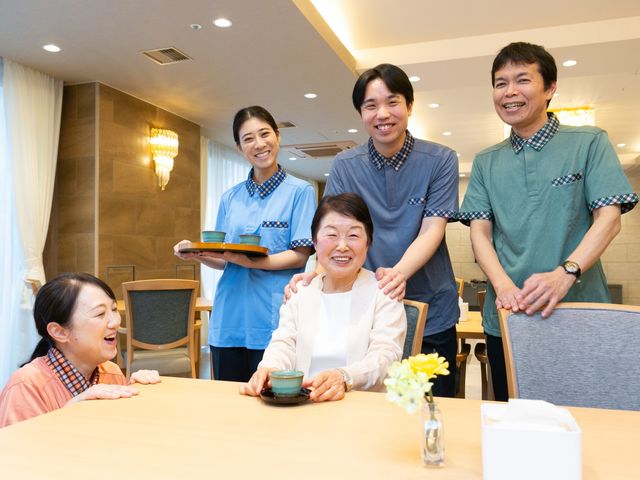 笑顔の職員と利用者の食堂 食堂   笑顔で接する職員と利用者の様子が伝わる食堂です。明るい照明とゆったりした席配置で、和やかな雰囲気が感じられます。