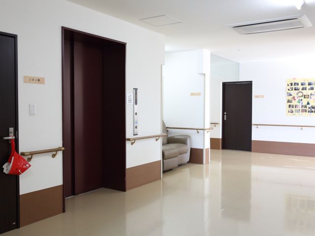 廊下の様子 エレベーター 清潔感のあふれる廊下が広がっており、手すりが整っていますので、歩行に不安がある方でも安心して移動できます。壁には、共同生活の楽しい様子が写った掲示物があり、温かい雰囲気を感じさせます。