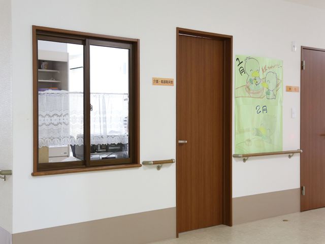 廊下の壁と扉 職員室 趣のある壁掛けが飾られた明るい廊下です。手すりが整っており、安全に移動できる設計になっています。