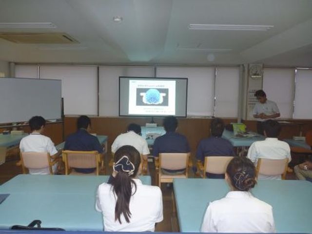 研修室で座る職員 多目的室   前方のスクリーンを見ながら着席している様子です。研修や勉強会に使いやすい、落ち着いた多目的室です。