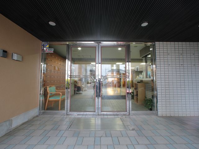 入口に人 玄関 ガラス扉を通じて光が差し込む開放感のあるエントランスです。心地よい待合スペースが設けられ、訪れる人を温かく迎えます。