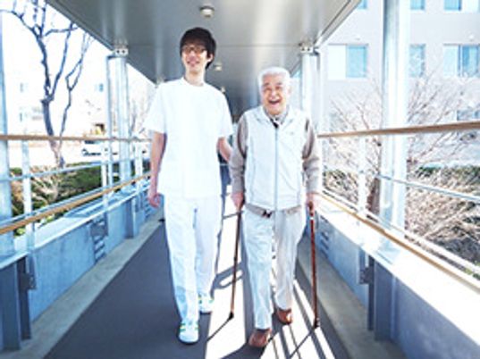 杖を突いて歩いている入居者様に、寄り添い肩を並べて歩いているスタッフ