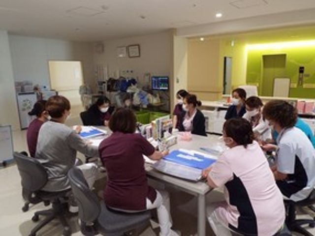 食堂で会議する人々 食堂   広い食堂で、スタッフの方々がテーブルを囲んで打ち合わせをしています。明るい空間で、連携しながら働く様子が伝わります。