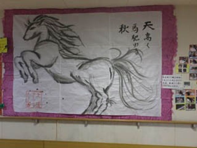 掲示物が飾られた廊下 掲示物 廊下の壁には力強い馬の絵が飾られており、落ち着いた雰囲気を醸し出しています。日々の暮らしに彩りを与える工夫が見受けられます。