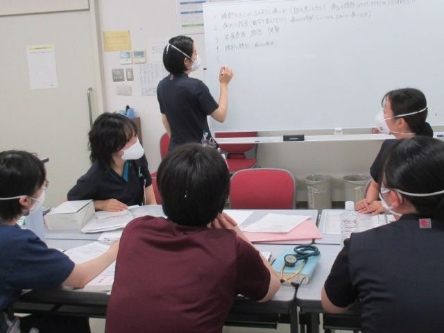 研修中の会議室 多目的室   マスクを着けたスタッフが集まり、ホワイトボードを使って打ち合わせをしています。学び合う場の雰囲気が伝わり、就業前の研修イメージがしやすいです。