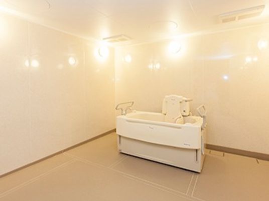 施設の写真 広い浴室内にリフト浴だけが置かれている。シャワーなどは見当たらない。内装はクリーム色を基調としたやわらかい色合い。