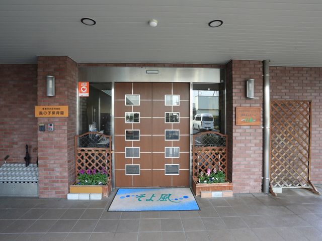入口と植物がある玄関 玄関前 暖かみのある色合いの壁と、清潔感あふれるエントランスです。訪れる人々を迎え入れるための配慮が行き届いています。