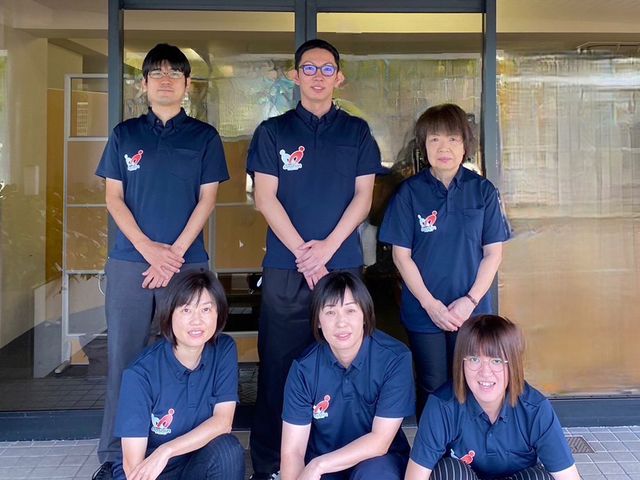 スタッフの集合写真 スタッフイメージ 笑顔で立つ職員さんたちが、温かい雰囲気を醸し出しており、訪れる皆さんを温かく迎え入れます。