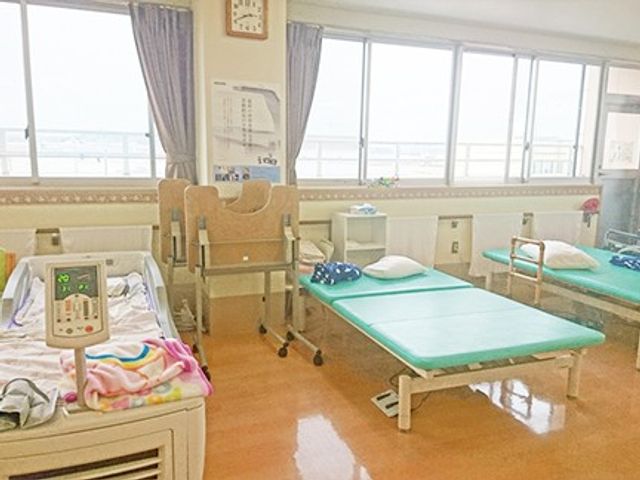 機能訓練室のベッドと歩行器 機能訓練室   窓から光が入る明るい空間で、ベッドや歩行器がゆとりをもって配置されています。訓練や休息に使いやすい環境が整っています。