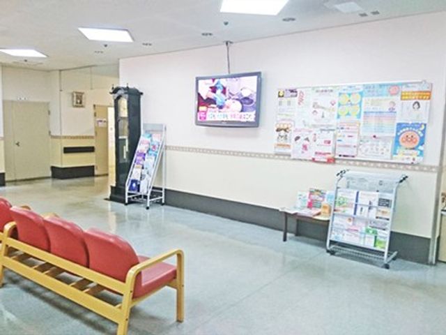 待合ベンチのある廊下 廊下   明るい廊下にベンチが置かれ、壁には掲示物とテレビが見えます。休憩しながら情報確認もしやすい空間です。