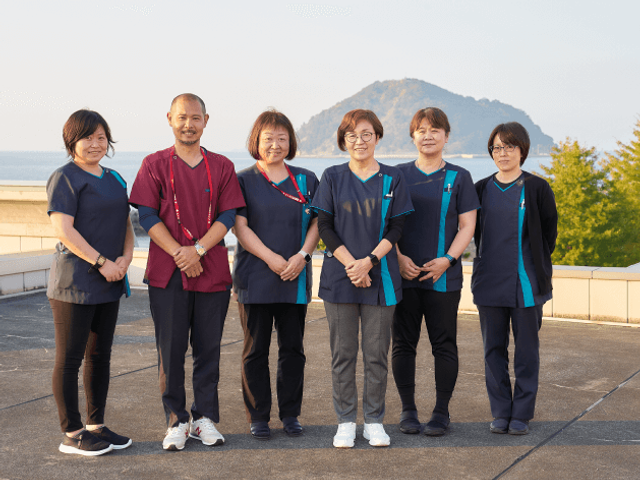 屋外で並ぶスタッフ スタッフイメージ   6人のスタッフが屋外に並んで立っています。明るい表情で整った装いが印象的です。