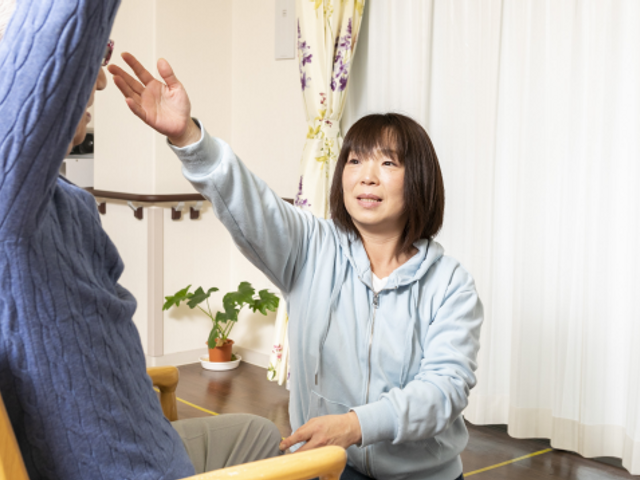 スタッフと利用者の手を合わせる様子 ケアの現場で、明るく親しみやすいスタッフが利用者とコミュニケーションを図っています。心温まる対話が日常的に行われる場です。