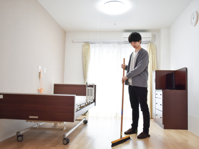 清掃する人と居室 広々とした清潔な居室で、スタッフが丁寧に掃除をしています。快適な環境を整えるお仕事に、あなたも一緒に取り組みませんか？