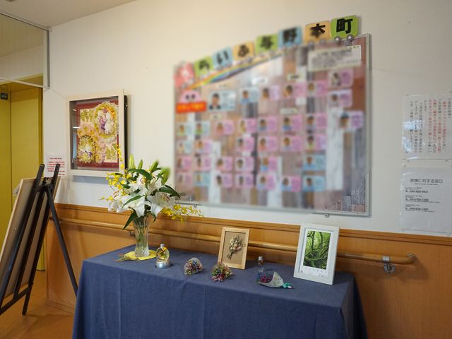 花と掲示物のロビー 展示物 ゆったりとした空間に彩られる花々が、日常の潤いをもたらしています。スタッフと利用者様のコミュニケーションの場としても機能している様子です。