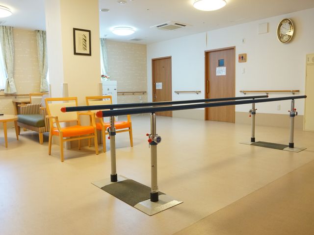 リハビリ訓練ができる部屋 機能訓練室 明るく開放的な空間で、歩行の安定を支援する平行棒が配されています。業務に携わる方にとって、利用者様の自立支援に役立つ設備が整っています。