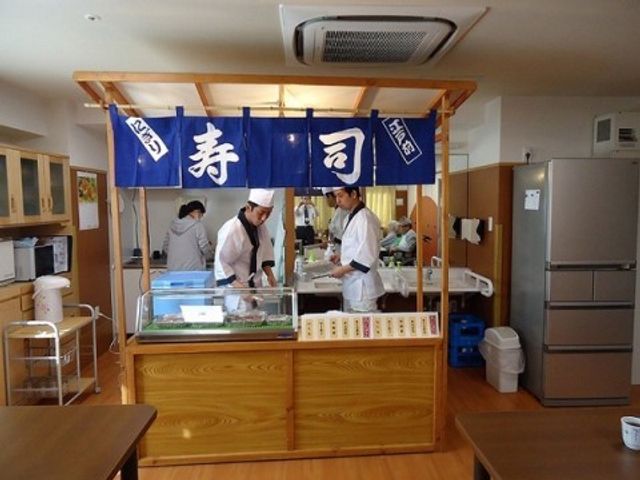 料理スタッフと厨房カウンター 寿司屋台 清潔感のある厨房で調理スタッフが真剣に作業をしています。新鮮な食材で栄養バランスを考えたお食事の提供に努めております。