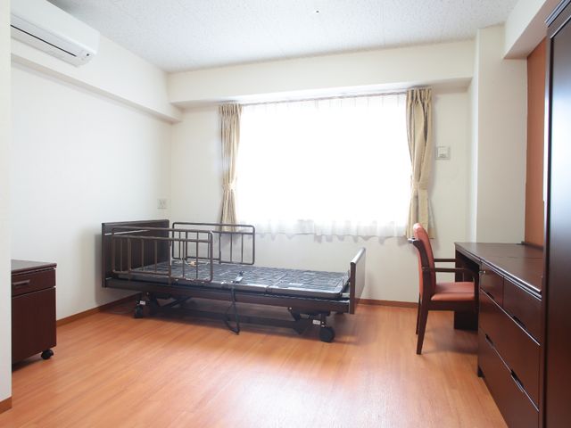 清潔な居室の一角 居室 床は木目調で、ベッドやデスクも整っています。癒しの空間を提供するために工夫されています。