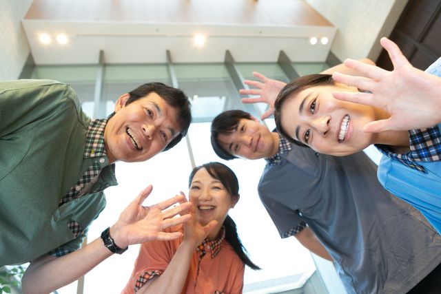 笑顔のスタッフ集合 スタッフイメージ   明るい空間で、スタッフの皆さんが笑顔で手を振っています。声をかけやすい雰囲気が伝わり、協力して働く様子が感じられます。