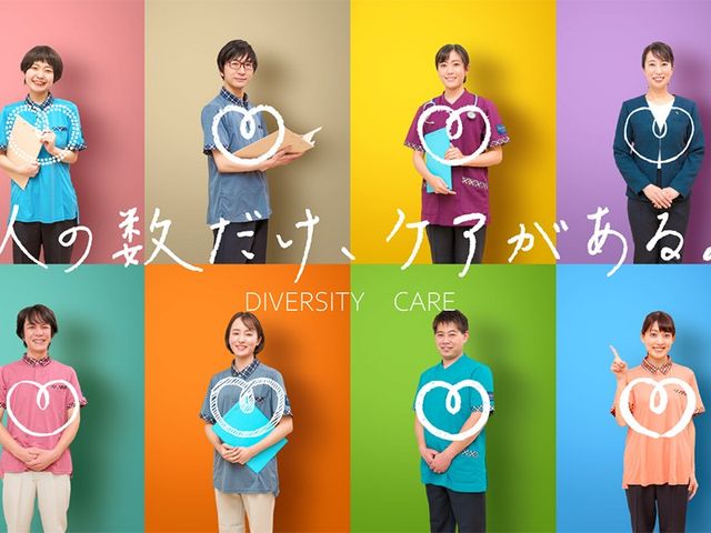 スタッフ集合ポートレート スタッフイメージ   明るい背景の前で、複数のスタッフの方が笑顔で並んでいます。介護の現場で働く人の雰囲気を知りたい方に参考になる一枚です。