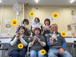 工作着の6人が制作物を持つ多目的室  