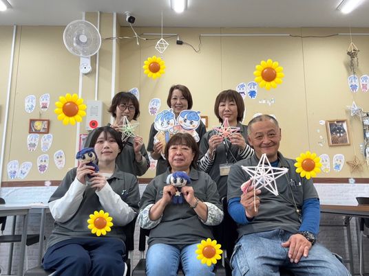 工作着の6人が制作物を持つ多目的室  