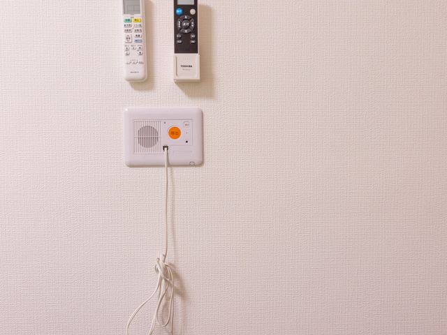 呼び出しボタンの壁面 居室   壁面に呼び出しボタンやリモコンが設置され、必要なときに使いやすい環境です。入居者の安全確認や対応のしやすさが伝わります。