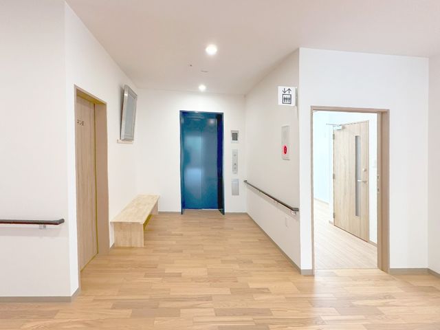 明るい廊下とエレベーター前 廊下   木目調の床と白い壁で、すっきりした印象の廊下です。手すりが左右にあり、移動しやすさに配慮されています。