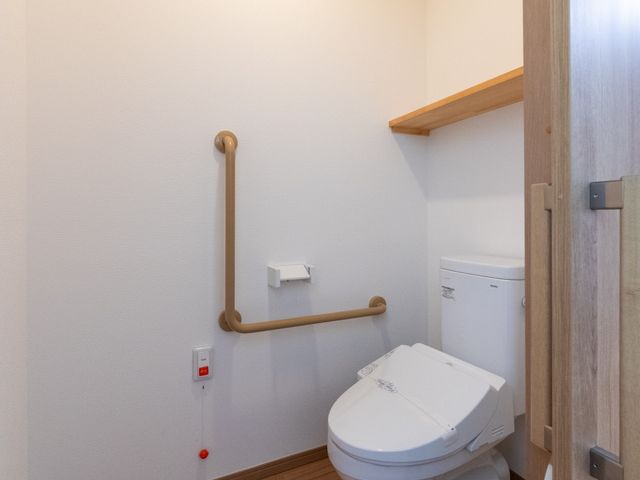 手すり付きトイレ トイレ 木目調の落ち着いた空間に手すりが設置されたトイレです。出入り口が広めで、使いやすさに配慮されています。