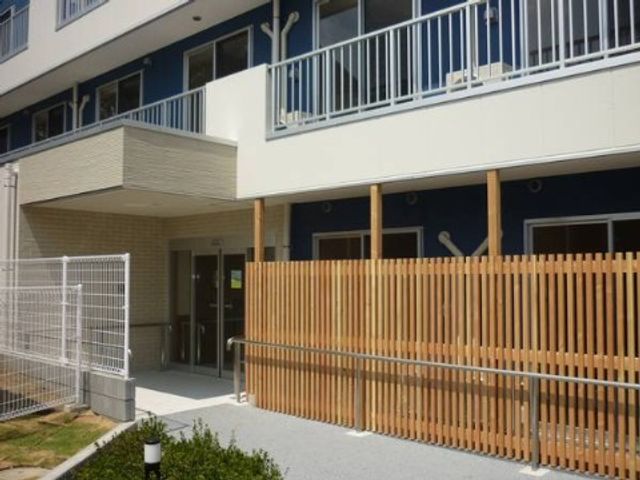 明るく開放的な施設外観 24時間サポート 陽光あふれる施設のエントランスは、清潔感があり安心感を与えるデザインになっています。利用者の方々の快適な毎日がここから始まります。