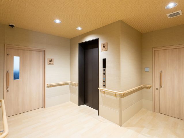 エレベーター付き廊下 エレベーター 明るい照明で安全面に配慮されたエレベーター付きの広い廊下です。通路には手すりが設置されています。