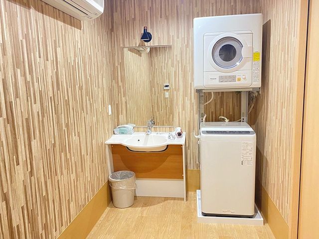 洗面台と洗濯機のある室内 洗面台   洗面台と乾燥機付き洗濯機が並ぶ、整理された空間です。清掃や洗濯の動線がまとまっていて、働く場としても使いやすそうです。
