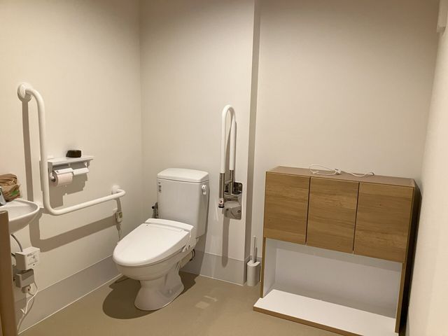 手すり付きトイレ トイレ   手すりが複数あり、立ち座りを支えやすいトイレです。木目の収納もあり、すっきりとした空間になっています。