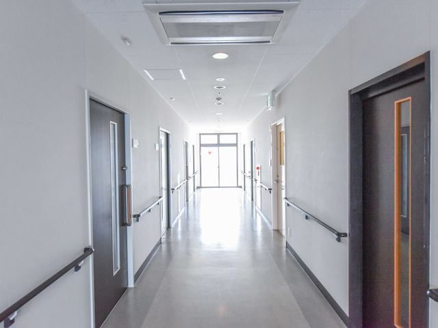 明るい施設の廊下 廊下 清潔感があり、明るい照明の下で安全に通行できる廊下です。手すりも完備しており、安心してご利用いただけます。